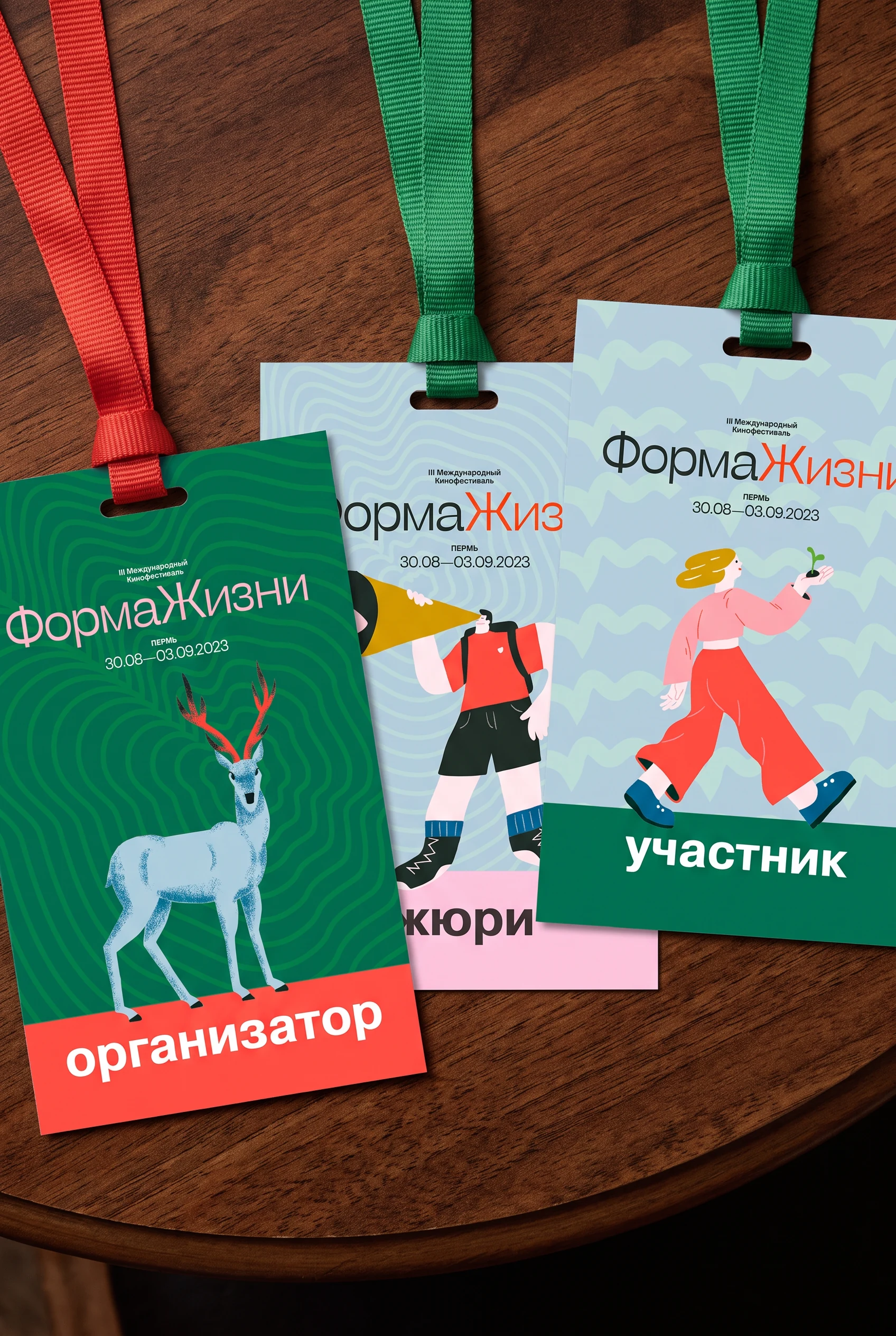 Three accreditation badges on lanyards — organiser, jury and participant — each on a different ground with its own painted figure.