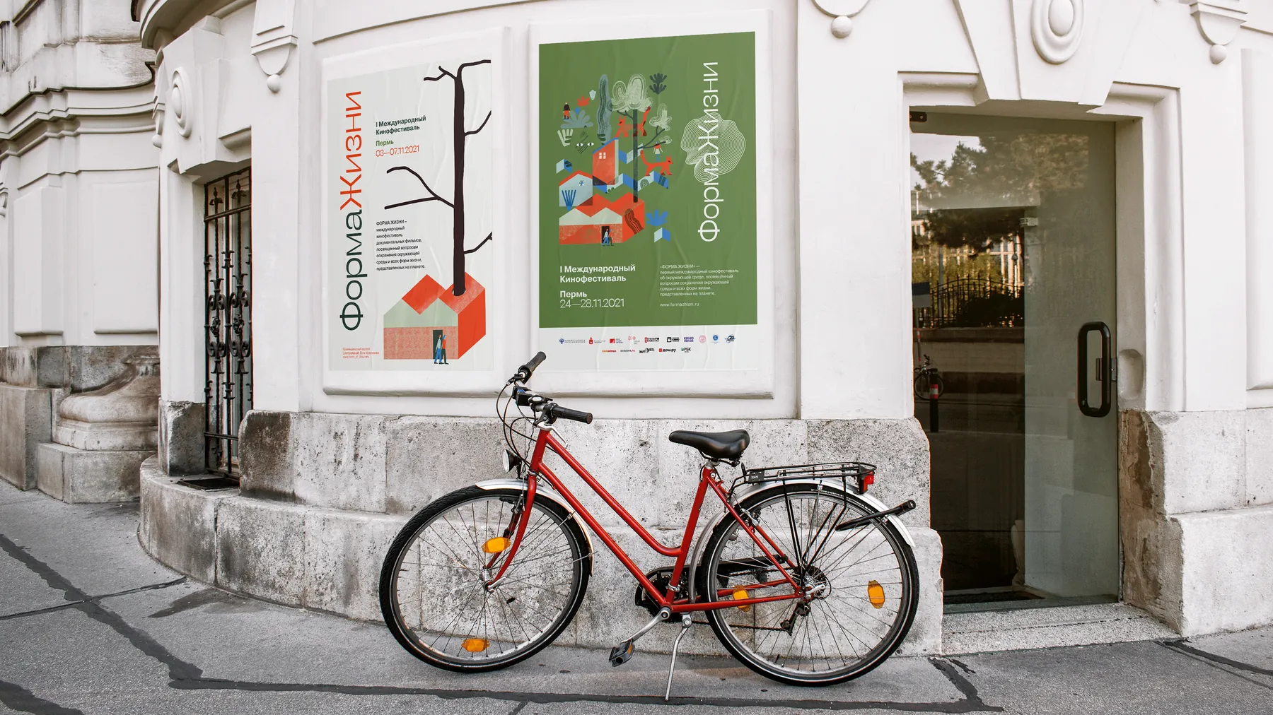 Two festival posters mounted on the facade of a white classical building, with a red bicycle parked below.